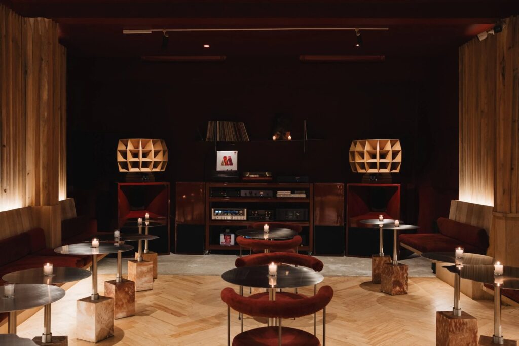 Sala principal de Shhh: bocinas de bocina múltiple de madera, rack central con tornamesa y amplificación, y mesas bajas